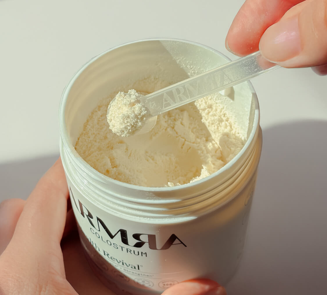 A scoop of ARMRA Colostrum powder lifted from the jar